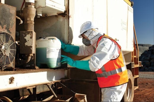 A worker in protective gear handling a chemical container at an industrial site.