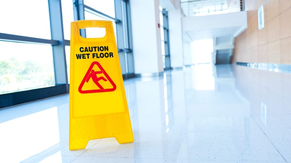 Caution wet floor sign in a brightly lit hallway, highlighting hazard control steps for preventing slips and falls